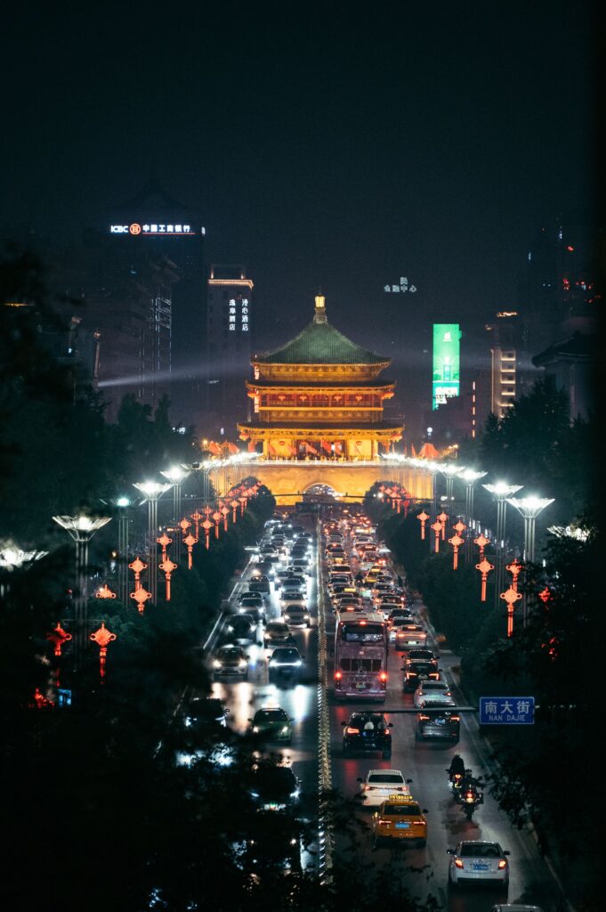 un templo chino de noche, alumbrado por luces doradas, pasan coches por debajo de el